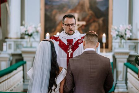 Valmiera, Letonia 28 de julio de 2024 - Un sacerdote con una estola bendice a una novia y un novio durante su ceremonia de boda en una iglesia.