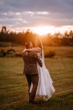 Photo for Valmiera, Latvia- July 28, 2023 - A bride and groom in a sunset embrace, with the groom's back to the camera and the bride smiling over his shoulder. - Royalty Free Image