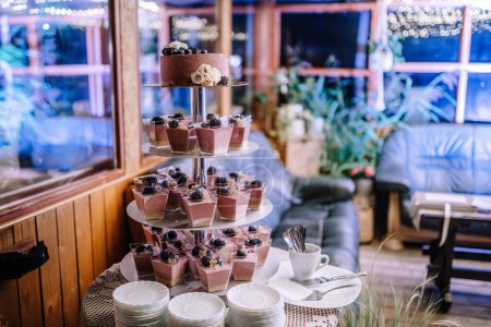 Foto de Valmiera, Letonia - 28 de julio de 2023 - Una exhibición de postres con una tarta estratificada y copas de mousse de chocolate cubiertas con bayas, ambientadas en una habitación con iluminación festiva. - Imagen libre de derechos
