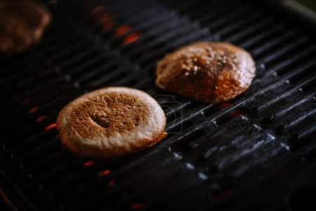 Valmiera, Latvia- July 29, 2023 - Burger buns are toasted on a grill with visible grill marks and glowing coals beneath them.