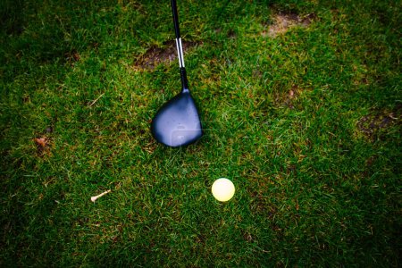 Close-up of a golf club about to hit a yellow golf ball on grass.