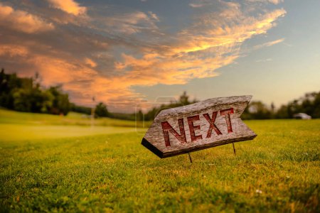 Sigulda, Latvia - July 30, 2023 - A rustic wooden sign with the word "NEXT" points to the right on a golf course with a sunset sky in the background.