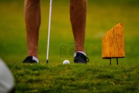 Foto de Sigulda, Letonia - 30 de julio de 2023 - Acercamiento de las piernas de un golfista por una pelota de golf y un palo, junto a un marcador de tee en el campo. - Imagen libre de derechos