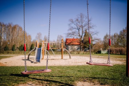 Valmiera, Latvia - April 21, 2024 - Empty swings on a playground with a clear blue sky and trees in the background, suggesting a peaceful outdoor scene.