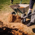 Valmiera, Latvia - April 21, 2024 - A person is shoveling soil into a wheelbarrow on a sunny day, showing a part of gardening or construction work.