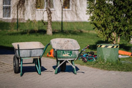 Téléchargez les photos : Valmiera, Lettonie - 21 avril 2024 - Deux brouettes en évidence avec du matériel de jardinage en arrière-plan, indiquant des travaux extérieurs ou de l'aménagement paysager. - en image libre de droit