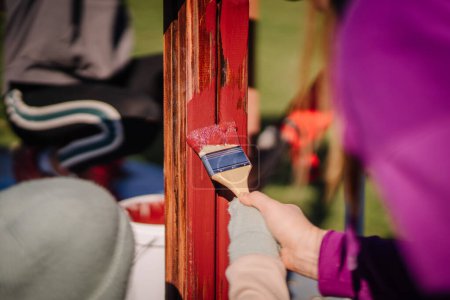 Valmiera, Latvia - April 21, 2024 - A close-up of a hand applying red paint to a wooden beam with a paintbrush, with a blurred background.