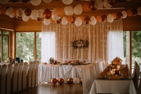 Foto de Valmiera, Letonia - 5 de agosto de 2023 - Elegante local de recepción de bodas interiores decorado con cortinas blancas, arreglos florales, velas y globos en tonos neutros. - Imagen libre de derechos