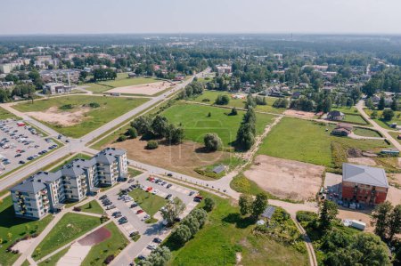 Valmiera, Latvia - August 7, 2023 - Overhead view of a mixed urban area showing apartment buildings, a parking lot, undeveloped land, a sports field, and a busy road.