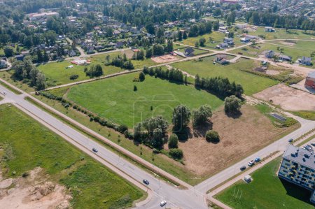 Foto de Valmiera, Letonia - 7 de agosto de 2023 - Aerial shot of a suburban development with roads, houses, a green field, and a construction site. - Imagen libre de derechos