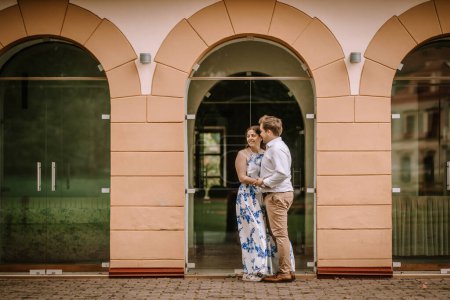 Couple s'embrassant et se souriant sous une arche avec réflexion dans les portes vitrées.