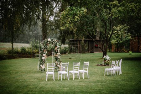 Photo for Valmiera, Latvia - August 10, 2023 - A floral wedding arch and white chairs set up on a lawn for a ceremony. - Royalty Free Image