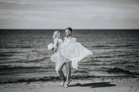 Photo for Valmiera, Latvia - August 10, 2023 - Groom lifting bride in a twirl on the beach, black and white photo. - Royalty Free Image