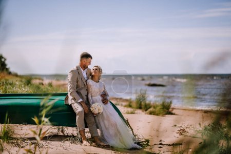 Photo for Valmiera, Latvia - August 10, 2023 -Bride and groom sitting on a boat at the beach, looking at each other lovingly. - Royalty Free Image