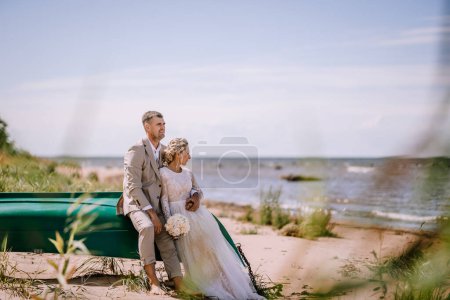 Foto de Valmiera, Letonia - 10 de agosto de 2023 - Novia y novio sentados en un barco en la playa - Imagen libre de derechos