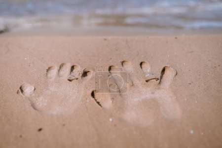 Valmiera, Latvia - August 10, 2023 - Handprints and wedding rings in the sand on a beach.