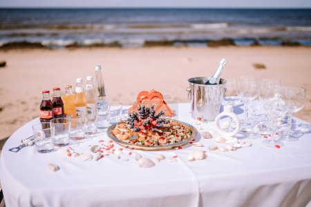 Photo for Valmiera, Latvia - August 10, 2023 - Beach wedding reception table with food platter, drinks, and champagne on white linen. - Royalty Free Image
