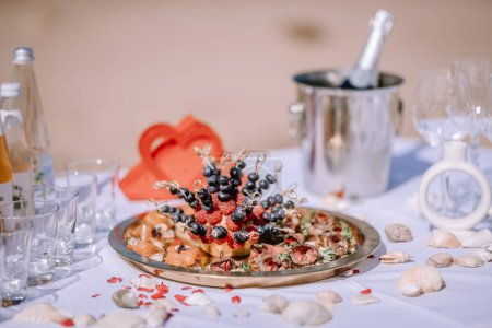 Valmiera, Latvia - August 10, 2023 - Close-up of a gourmet beach table setup with a platter of berries, meats, and a champagne bucket.
