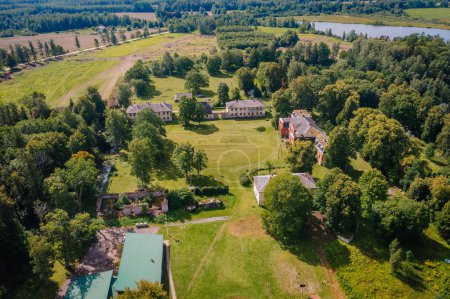 Valmiera, Latvia - August 10, 2023 - Aerial view of Katvaru manor with surrounding greenery and distant river.