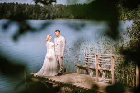 Photo for Valmiera, Latvia - August 10, 2023 - Bridal couple standing on a dock by a serene lake, surrounded by forest, exchanging a loving glance. - Royalty Free Image