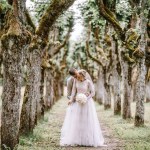 Valmiera, Latvia - August 10, 2023 - A wedding couple embracing among a moss-covered avenue of trees.