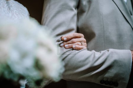 Valmiera, Latvia - August 10, 2023 - Close-up of a groom's hand touching the bride's back, both in wedding attire.