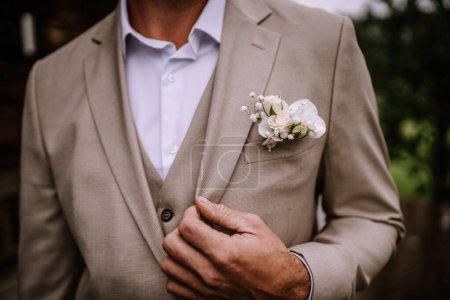 Photo for Valmiera, Latvia - August 10, 2023 - A groom adjusting his beige suit jacket with a white boutonniere. - Royalty Free Image