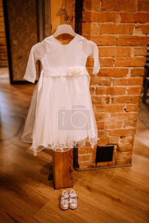 Valmiera, Latvia - August 10, 2023 - A white dress and matching shoes for a child displayed in front of a brick wall.