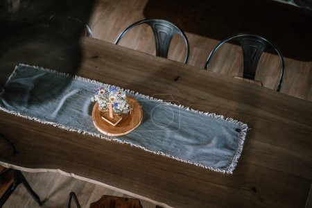 Valmiera, Latvia - August 10, 2023 - Overhead view of a wooden dining table with a blue runner and a small vase with wildflowers.