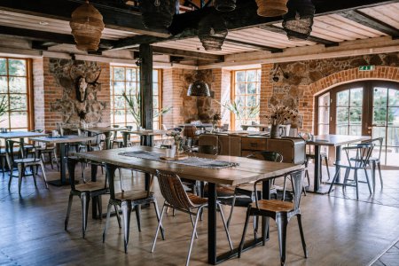 Valmiera, Latvia - August 10, 2023 - Interior of a rustic restaurant with wooden tables, chairs, and wicker lamps, and stone walls.