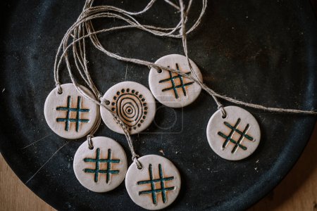 Valmiera, Latvia - August 10, 2023 - Ceramic pendants with symbols and patterns on a twine string, placed on a dark plate.