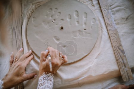 Valmiera, Latvia - August 10, 2023 - Hands carving into clay with footprints and handprints, on a floured surface with wooden tools.
