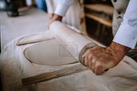 Valmiera, Lettonie - 10 août 2023 - Gros plan sur les mains déroulant la pâte avec un rouleau à pâtisserie en bois sur une surface farinée.