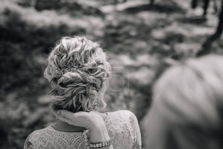 Valmiera, Latvia - August 10, 2023 - Close-up of a bride's hairstyle from the back, hand touching her hair, outdoors.