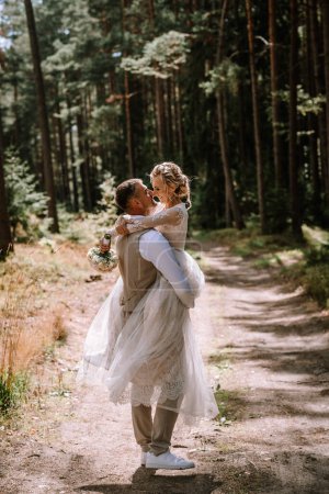 Photo for Valmiera, Latvia - August 10, 2023 - Groom lifting bride in his arms in a forest setting, both smiling and looking at each other. - Royalty Free Image