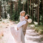 Valmiera, Latvia - August 10, 2023 - Groom lifting bride in his arms in a forest setting, both smiling and looking at each other.