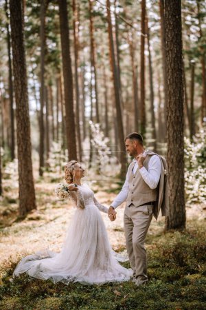 Valmiera, Latvia - August 10, 2023 - Wedding couple standing in a forest, looking at each other, with the bride holding a bouquet.