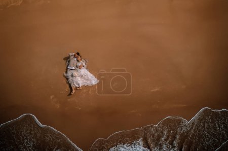 Photo for Valmiera, Latvia - August 10, 2023 - Aerial view of a wedding couple embracing on a sandy beach with waves approaching. - Royalty Free Image