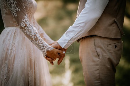 Valmiera, Letonia - 10 de agosto de 2023 - Acercamiento de una novia y un novio tomados de la mano, enfoque en las manos y el atuendo de boda.