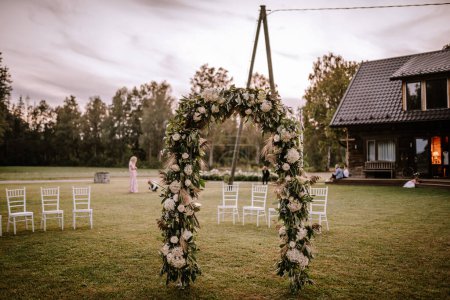Valmiera, Lettland - 10. August 2023 - Torbogen an einem Hochzeitsort im Freien mit leeren Stühlen und Menschen im Hintergrund.