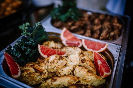 Valmiera, Latvia - August 10, 2023 - Grilled chicken breast slices with grapefruit wedges and kale garnish in a serving tray.