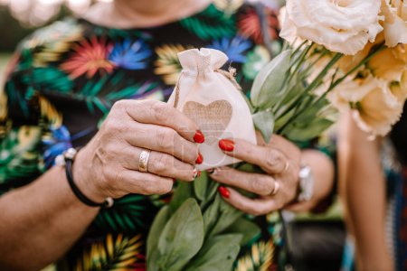 Valmiera, Latvia - August 10, 2023 - Close-up of hands holding a small fabric pouch with a heart, flowers in the background.
