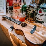 Valmiera, Latvia - August 10, 2023 - Ukulele on a bar counter with bottles of alcohol and a cocktail in the background.