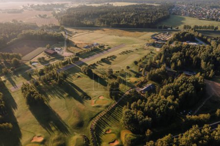 Valmiera, Latvia - August 12, 2023 - Sunlit aerial view of a 9-hole golf course with a driving range and surrounding forest.