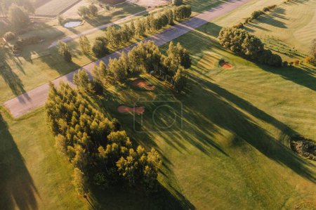 Foto de Valmiera, Letonia - 12 de agosto de 2023 - Hora dorada en un campo de golf con largas sombras, árboles y trampas de arena. - Imagen libre de derechos