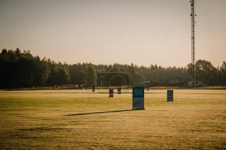 Foto de Valmiera, Letonia - 12 de agosto de 2023 - Temprano en la mañana en un campo de prácticas con marcadores de distancia y una torre de radio en el fondo. - Imagen libre de derechos