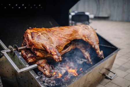 Dobele, Latvia - August 18, 2023 - A whole pig being roasted on a large barbecue grill with a person standing behind.
