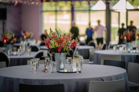 Foto de Dobele, Letonia - 18 de agosto de 2023 - La pieza central floral en una mesa de eventos con invitados y más mesas en el fondo. - Imagen libre de derechos