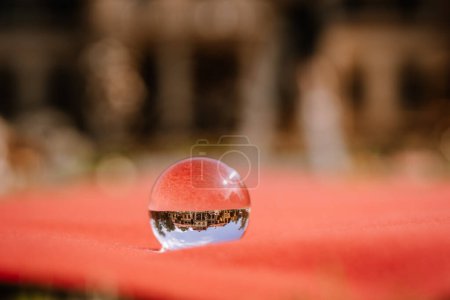Valmiera, Lettonie - 19 août 2023 - Une boule de cristal se trouve sur une surface rouge, capturant un reflet inversé d'un bâtiment, entouré d'un arrière-plan flou.