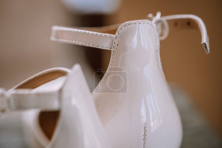 Valmiera, Latvia - August 19, 2023 - Close-up of elegant white high-heeled bridal shoes with a glossy finish and fine stitching detail, set against a soft background.